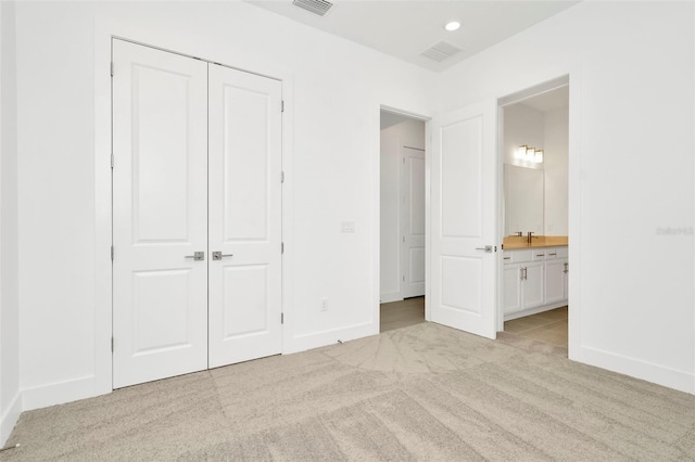 unfurnished bedroom with a closet, light colored carpet, ensuite bathroom, and baseboards