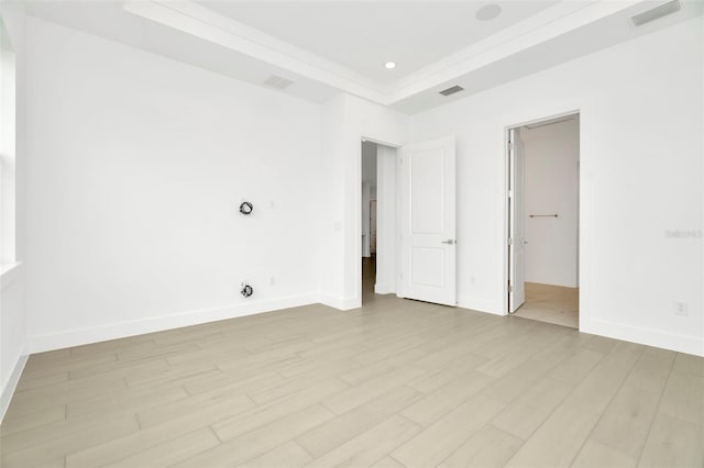 empty room with visible vents, a raised ceiling, baseboards, and light wood-style flooring