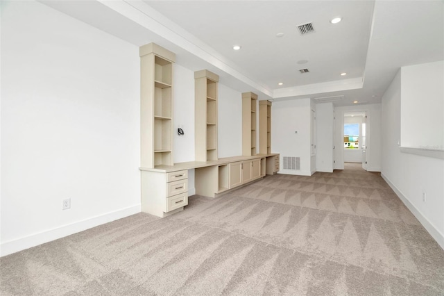 unfurnished living room with light carpet, visible vents, built in study area, and a raised ceiling