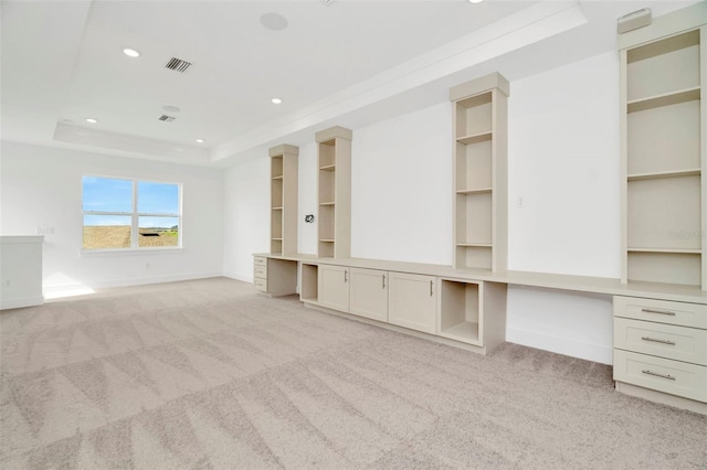 unfurnished living room with a tray ceiling, built in desk, and carpet flooring