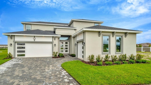 prairie-style home with stucco siding, decorative driveway, a front yard, and an attached garage