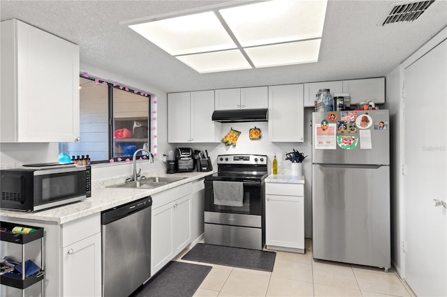 kitchen with a textured ceiling, light tile patterned floors, appliances with stainless steel finishes, sink, and white cabinetry