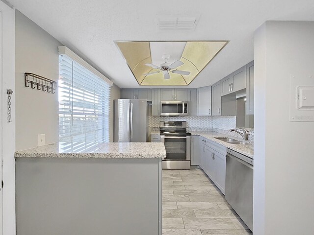 kitchen featuring stainless steel appliances, kitchen peninsula, gray cabinets, decorative backsplash, and ceiling fan