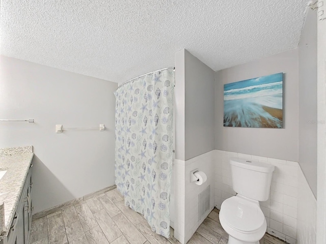 bathroom featuring toilet, tile walls, a shower with curtain, vanity, and a textured ceiling