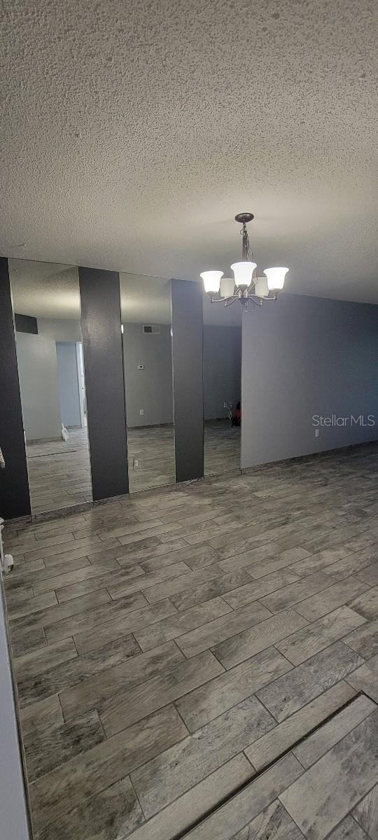 empty room featuring wood-type flooring, a chandelier, and a textured ceiling