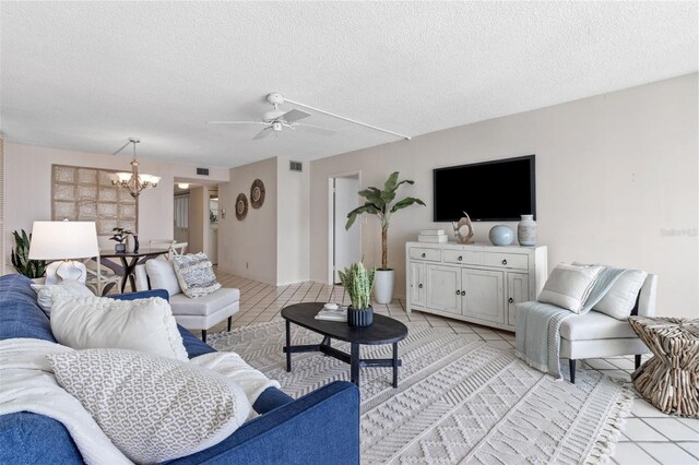 tiled living room featuring ceiling fan with notable chandelier and a textured ceiling