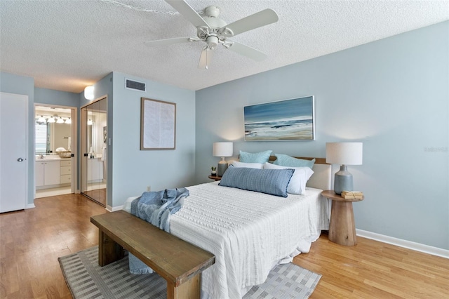 bedroom with a textured ceiling, light hardwood / wood-style flooring, ensuite bath, and ceiling fan