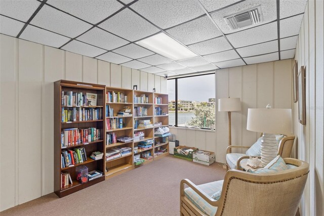 living area with a paneled ceiling and carpet flooring