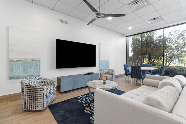 living room with a wall of windows, hardwood / wood-style floors, ceiling fan, and a drop ceiling