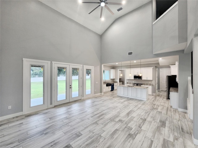 unfurnished living room with light hardwood / wood-style floors, ceiling fan, and high vaulted ceiling