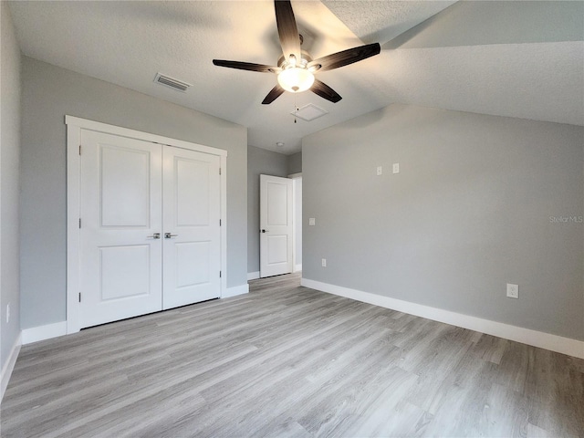 unfurnished bedroom featuring a textured ceiling, lofted ceiling, and light hardwood / wood-style flooring