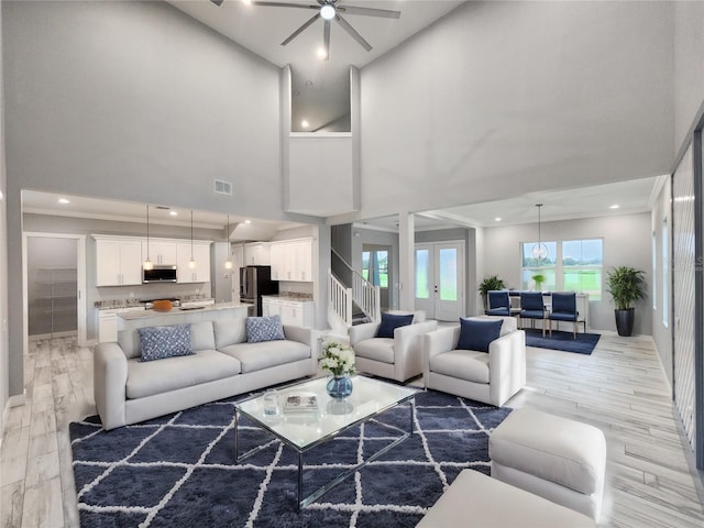 living room featuring ceiling fan, a towering ceiling, and light hardwood / wood-style floors