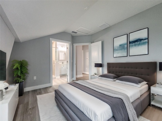 bedroom with light hardwood / wood-style flooring, connected bathroom, and vaulted ceiling