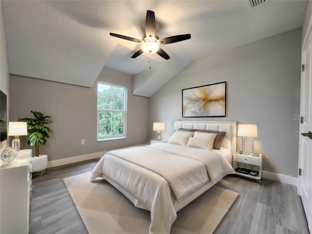 bedroom with ceiling fan, a textured ceiling, vaulted ceiling, and hardwood / wood-style flooring