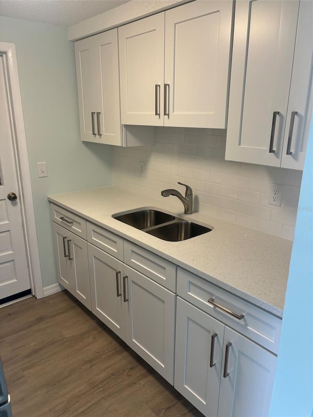 kitchen featuring backsplash, light stone countertops, white cabinetry, sink, and dark wood-type flooring