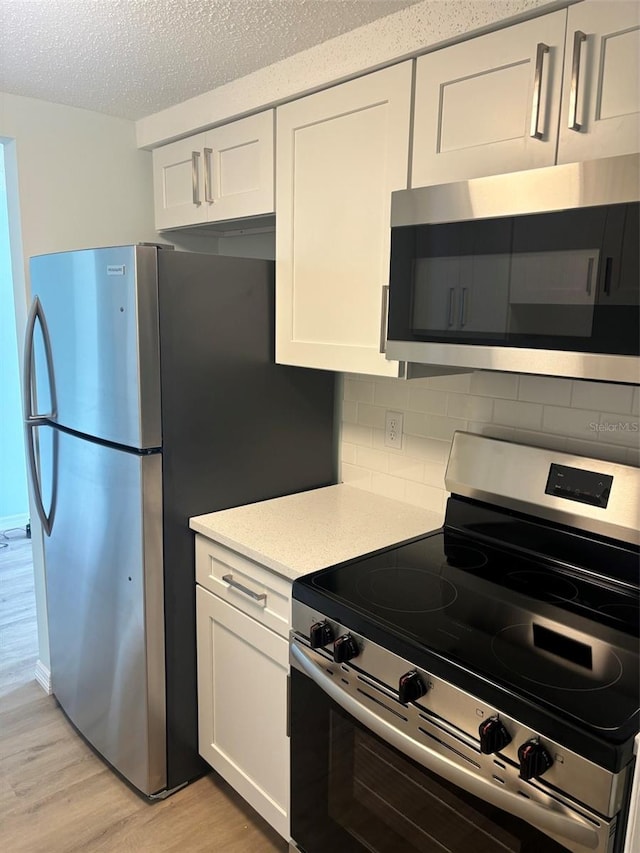 kitchen featuring tasteful backsplash, stainless steel appliances, white cabinetry, and light hardwood / wood-style flooring