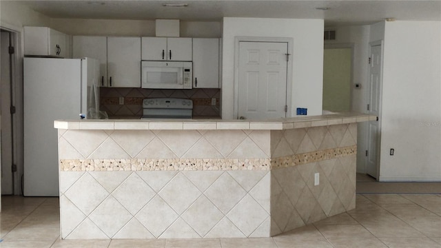 kitchen featuring tasteful backsplash, white cabinets, light tile patterned flooring, and white appliances