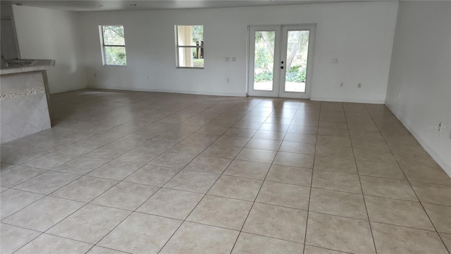 unfurnished living room featuring a healthy amount of sunlight, light tile patterned flooring, and french doors