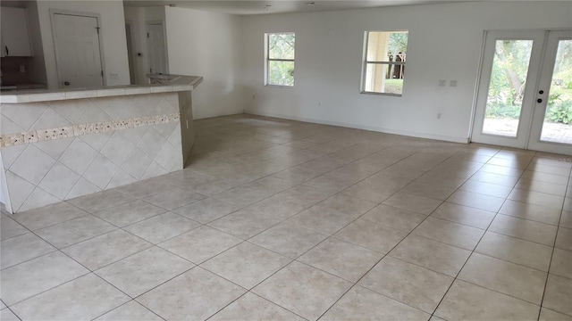 unfurnished living room featuring a healthy amount of sunlight, light tile patterned floors, and french doors