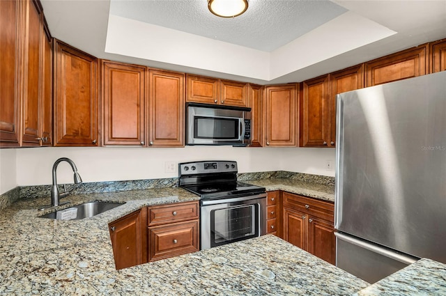 kitchen with light stone countertops, stainless steel appliances, sink, a tray ceiling, and a textured ceiling