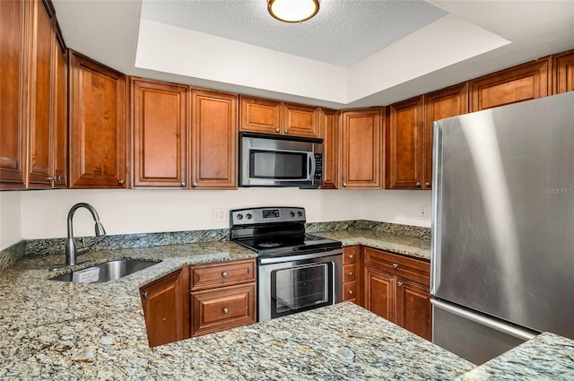 kitchen with light stone countertops, a tray ceiling, appliances with stainless steel finishes, a textured ceiling, and a sink