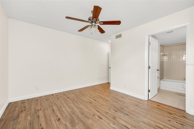 unfurnished bedroom featuring ceiling fan, a textured ceiling, ensuite bath, and light hardwood / wood-style flooring