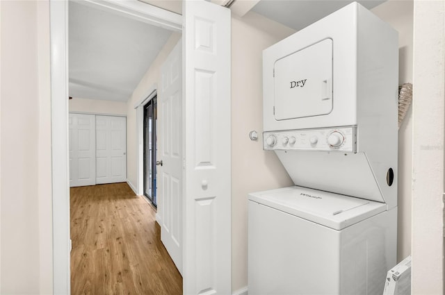 laundry room with light wood-style floors, baseboards, stacked washer and dryer, and laundry area