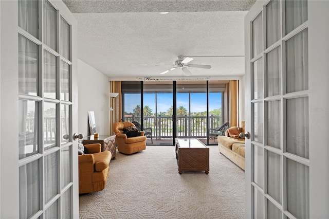 living room featuring light colored carpet, expansive windows, ceiling fan, and a textured ceiling