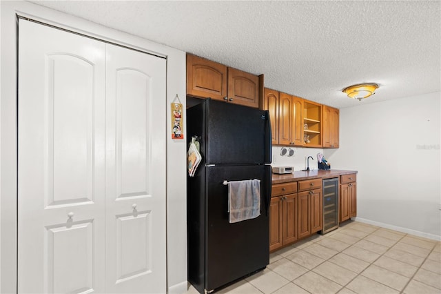 kitchen featuring a textured ceiling, beverage cooler, light tile patterned flooring, and black fridge