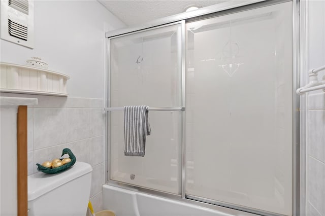 bathroom featuring tile walls, toilet, bath / shower combo with glass door, and a textured ceiling