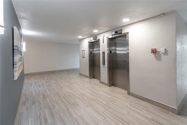 interior space featuring a textured ceiling, elevator, and light wood-type flooring