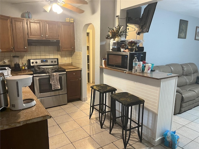 kitchen featuring light tile patterned floors, backsplash, appliances with stainless steel finishes, a kitchen bar, and ceiling fan