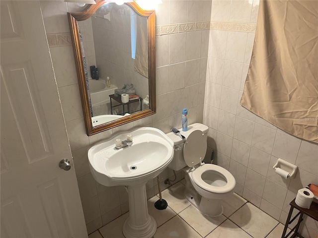 bathroom with toilet, tile patterned floors, a tub to relax in, sink, and tile walls