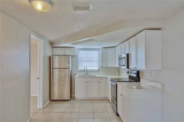 kitchen with appliances with stainless steel finishes, white cabinetry, light tile patterned floors, a textured ceiling, and sink