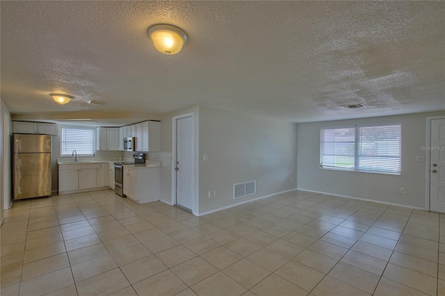 unfurnished living room featuring a textured ceiling, sink, and light tile patterned floors