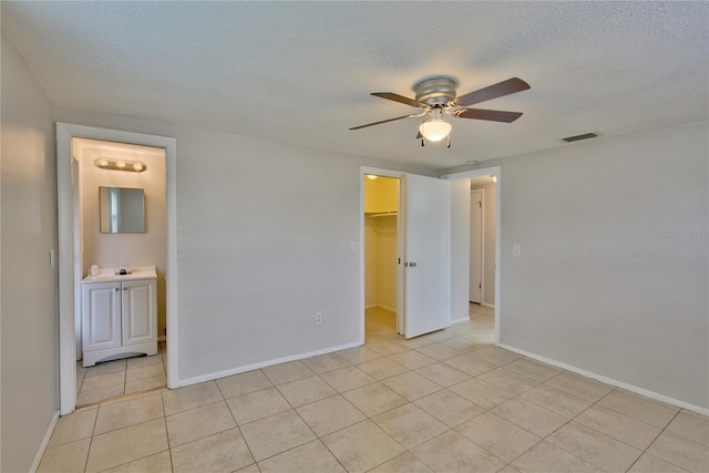 unfurnished bedroom with a spacious closet, a closet, a textured ceiling, ceiling fan, and ensuite bath