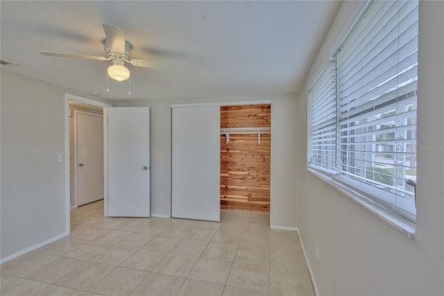 unfurnished bedroom featuring light tile patterned floors, wooden walls, ceiling fan, and a closet