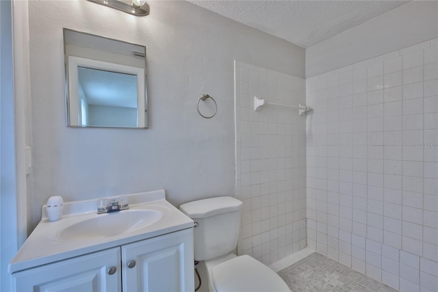 bathroom with a textured ceiling, a tile shower, vanity, and toilet