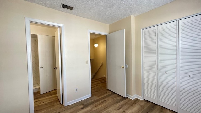 unfurnished bedroom featuring a closet, visible vents, a textured ceiling, and wood finished floors