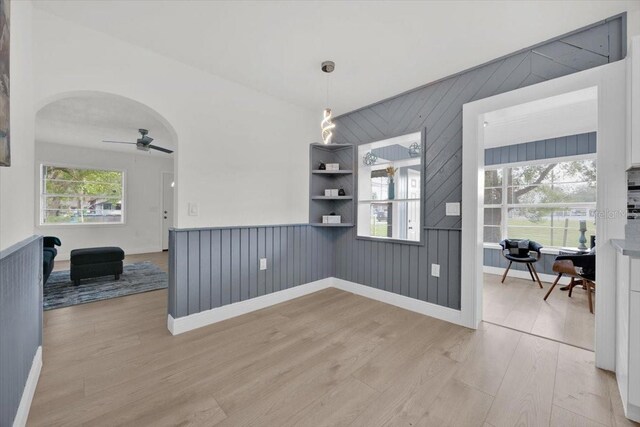 spare room featuring wooden walls, ceiling fan, light hardwood / wood-style floors, and plenty of natural light