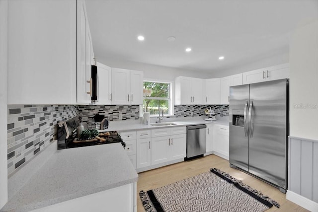 kitchen with tasteful backsplash, sink, light wood-type flooring, stainless steel appliances, and white cabinets