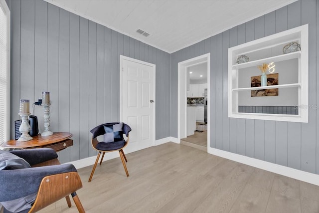 living area featuring ornamental molding, wooden walls, and light wood-type flooring