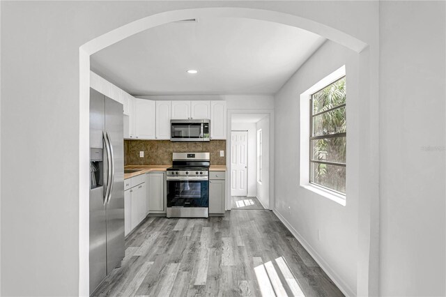 kitchen featuring light hardwood / wood-style flooring, appliances with stainless steel finishes, white cabinets, and decorative backsplash