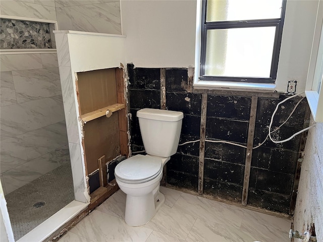 bathroom with a tile shower, tile walls, and toilet