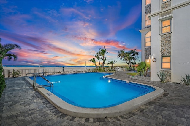 pool at dusk with a water view and a patio