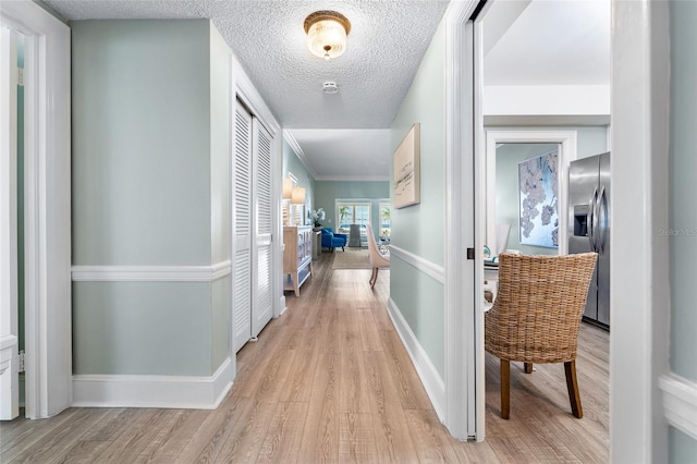 corridor with light hardwood / wood-style floors, a textured ceiling, and ornamental molding