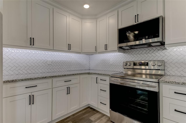 kitchen with light stone countertops, appliances with stainless steel finishes, decorative backsplash, white cabinetry, and hardwood / wood-style flooring