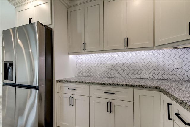 kitchen with light stone countertops, tasteful backsplash, white cabinets, and stainless steel refrigerator with ice dispenser