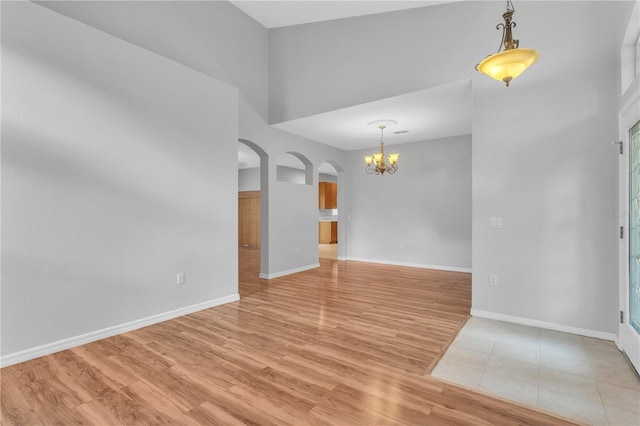 unfurnished room featuring hardwood / wood-style flooring, a chandelier, and a towering ceiling