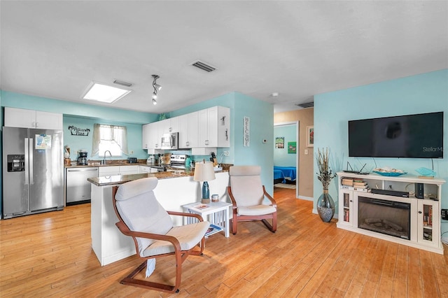 kitchen with white cabinetry, kitchen peninsula, stainless steel appliances, light hardwood / wood-style flooring, and sink